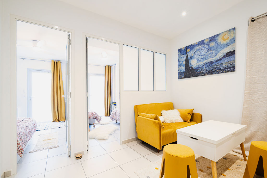 Appartement comportant un salon avec un canapé lit, une table et des chaises. Deux chambres sont visibles en arrière plan par des portes ouvertes.